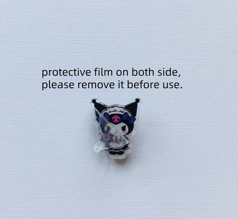 Op de afbeelding: Een heldere acryl bedel met een stripfiguur met zwarte oren, een roze gezicht en blauwe strikken. De bedel heeft een beschermfolie, met de tekst "protective film on both side, please remove it before use."