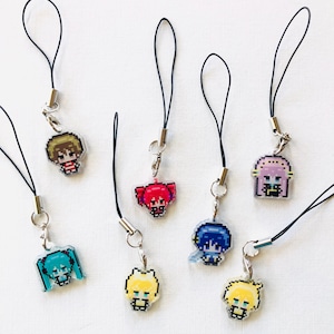 Puede incluir: Una colecci&oacute;n de siete dijes de personajes en pixel art unidos a bucles de cord&oacute;n negro con cierres de metal plateado. Cada dije presenta una figura de estilo anime con colores de cabello distintos, incluyendo turquesa, rubio, rosa, azul y marr&oacute;n, en un dise&ntilde;o de cuadr&iacute;cula.