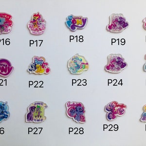 May include: A set of 10 colorful, clear plastic charms featuring My Little Pony characters. The charms are arranged in a grid pattern on a white background. Each charm has a different character and design, including a pink pony with a rainbow mane, a purple pony with a blue mane, and a yellow pony with a pink mane.