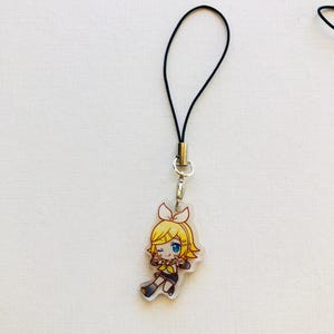 Peut inclure: Un charm en acrylique transparent repr&eacute;sentant un personnage de dessin anim&eacute; aux cheveux jaunes, aux yeux bleus et v&ecirc;tu d'une tenue noire et jaune. Le charm est attach&eacute; &agrave; un cordon noir avec un fermoir argent&eacute;. Le charm mesure environ 4 cm de hauteur.