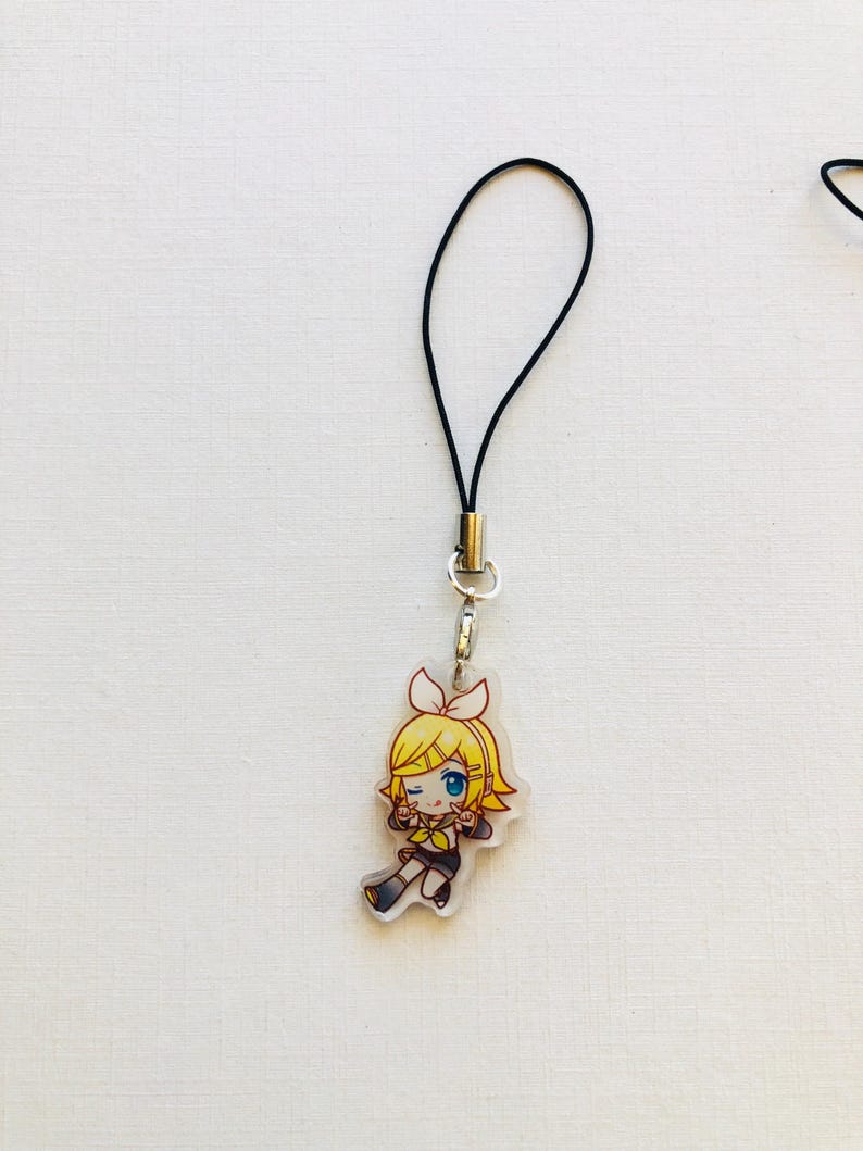 Peut inclure: Un charm en acrylique transparent repr&eacute;sentant un personnage de dessin anim&eacute; aux cheveux jaunes, aux yeux bleus et v&ecirc;tu d'une tenue noire et jaune. Le charm est attach&eacute; &agrave; un cordon noir avec un fermoir argent&eacute;. Le charm mesure environ 4 cm de hauteur.