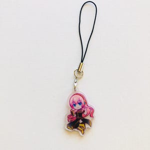Peut inclure: Un charm en acrylique transparent repr&eacute;sentant un personnage d'anime de style chibi aux cheveux roses et aux yeux bleus, v&ecirc;tu d'une tenue noire et dor&eacute;e. Le charm est attach&eacute; &agrave; un cordon noir avec un fermoir en m&eacute;tal argent&eacute;.