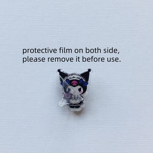 May include: A black and white character with a skull and crossbones design, wearing a blue and white bow, is shown on a clear acrylic charm. The charm has a protective film on both sides, with the text "protective film on both side, please remove it before use."