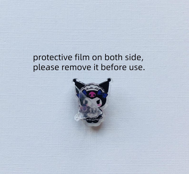 May include: A black and white character with a skull and crossbones design, wearing a blue and white bow, is shown on a clear acrylic charm. The charm has a protective film on both sides, with the text "protective film on both side, please remove it before use."