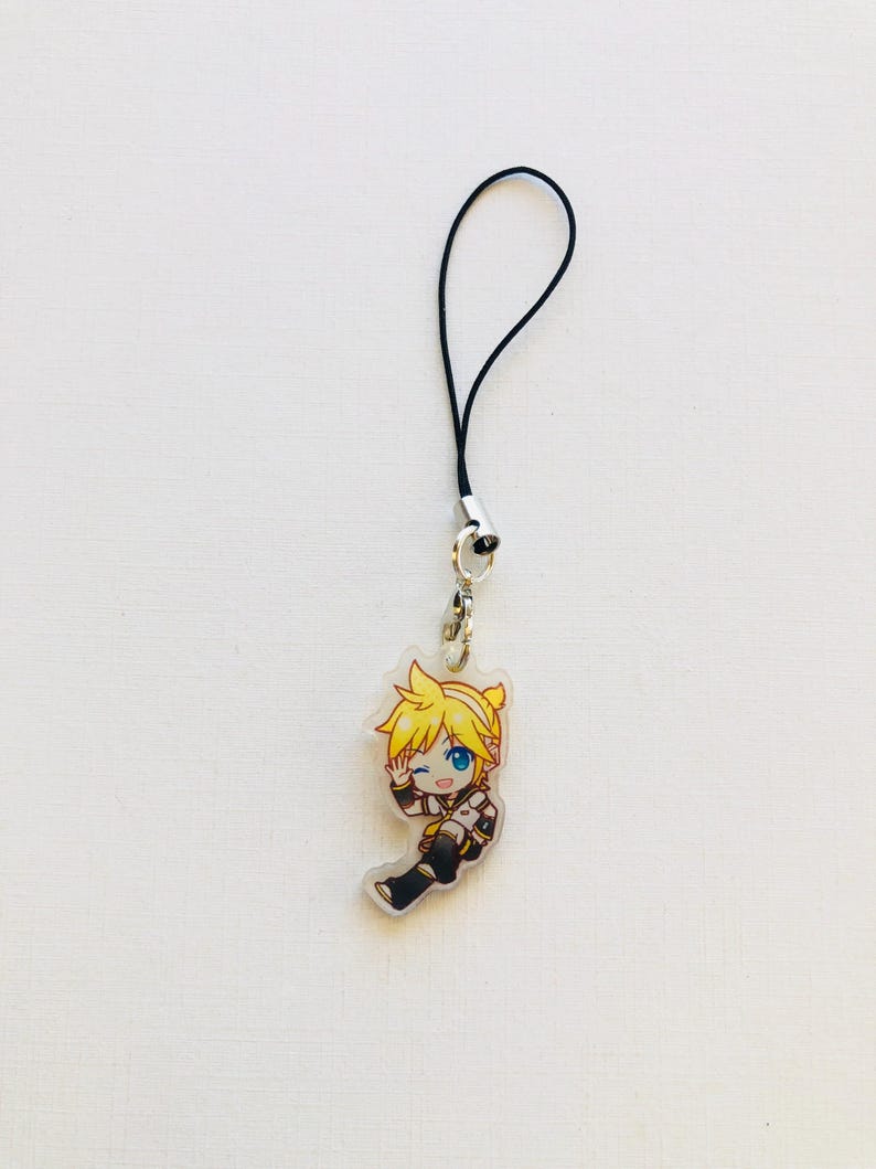 Peut inclure: Un charm en acrylique transparent repr&eacute;sentant un personnage de dessin anim&eacute; aux cheveux jaunes et aux yeux bleus, faisant un clin d'&oelig;il. Le charm est attach&eacute; &agrave; un cordon noir avec un fermoir argent&eacute;. Le personnage porte une tenue noire et blanche.