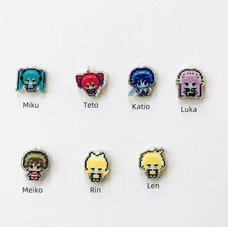Puede incluir: Siete peque&ntilde;os colgantes de acr&iacute;lico con personajes en arte de p&iacute;xeles. Los personajes est&aacute;n etiquetados como Miku, Teto, Katio, Luka, Meiko, Rin y Len. Cada colgante muestra un personaje &uacute;nico con colores de cabello distintos que incluyen verde azulado, rojo, azul, rosa, marr&oacute;n y amarillo.