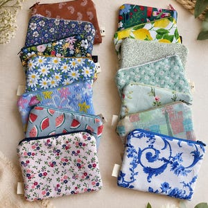May include: A collection of small, zippered pouches with various floral and patterned designs. The pouches feature a range of colors, including blue, pink, green, and brown. Some pouches have daisy, watermelon, and lemon prints. Each pouch has a small white tag.