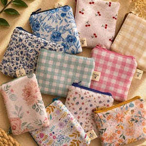 May include: A collection of ten small fabric zipper pouches featuring various patterns including blue floral, pink cherry, beige gingham, light blue gingham, pink gingham, and multi-colored floral prints, each with a small handmade tag attached.
