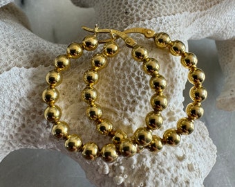 May include: Gold hoop earrings with a beaded design. The earrings are made of small, round gold beads.