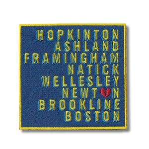 May include: Blue embroidered patch with yellow stitching. The patch features the names of towns in Massachusetts, including Hopkinton, Ashland, Framingham, Natick, Wellesley, Newton, Brookline, and Boston. A red broken heart appears next to the word "Newton".