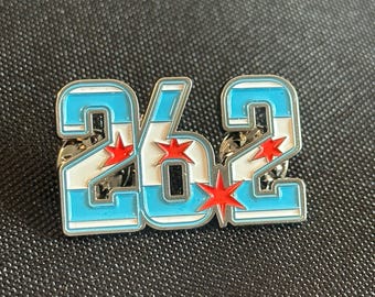 May include: A pin featuring the number "262" in a bold, stylized font. The numbers are white with light blue stripes and red star accents, set against a silver metal border. The pin is designed to be attached to clothing or accessories.