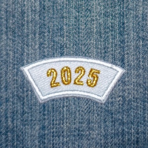 Könnte beinhalten: Weißer Patch mit einer goldenen Stickerei '2025' auf blauem Jeansstoff.