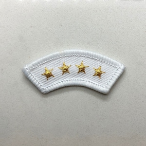 Puede incluir: Parche de tela blanco con cuatro estrellas doradas bordadas en una fila curva.