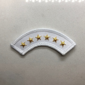 Puede incluir: Parche de tela blanco con forma curva y siete estrellas doradas bordadas.