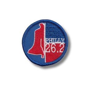 May include: A blue and red circular embroidered patch with a white outline. The patch features a red silhouette of the Liberty Bell and the text "PHILLY 26.2" in white.
