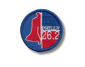 Peut inclure: Un écusson brodé circulaire bleu et rouge avec un contour blanc. L'écusson représente une silhouette rouge de la Liberty Bell et le texte "PHILLY 26.2" en blanc.
