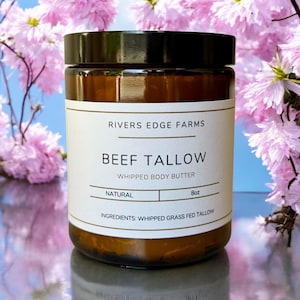 Peut inclure: Un pot en verre brun avec un couvercle noir contenant un beurre corporel fouetté au suif de bœuf naturel. Le pot est doté d'une étiquette blanche avec des lettres dorées qui indiquent "Rivers Edge Farms", "Beef Tallow", "Whipped Body Butter", "Natural", "8oz" et "Ingrédients : Suif de bœuf nourri à l'herbe fouetté".