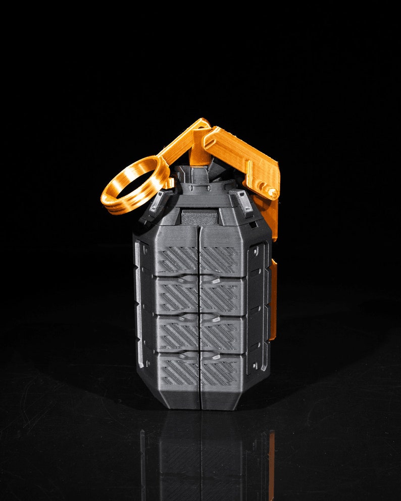 May include: A black and gold grenade-shaped object with a textured surface and a ring pull. The object is made of plastic and has a realistic appearance.