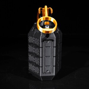 May include: A black and gold grenade replica with a textured surface and a pull ring. The grenade is on a black background.