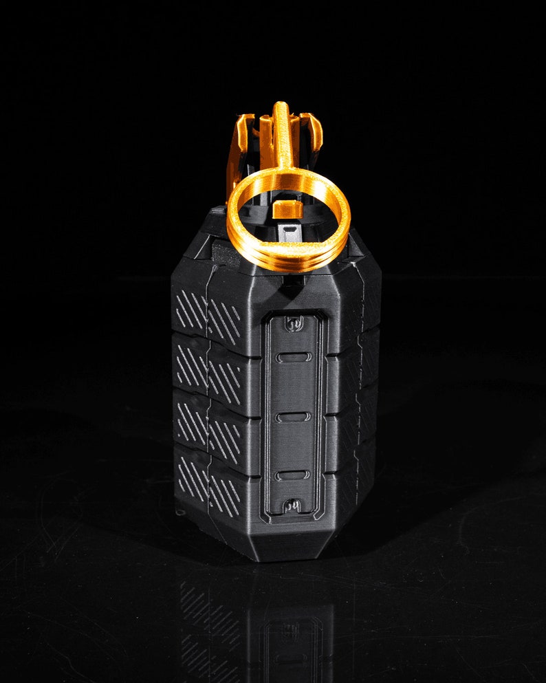 May include: A black and gold grenade replica with a textured surface and a pull ring. The grenade is on a black background.