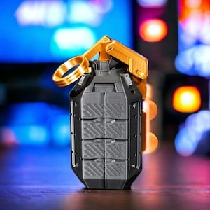 May include: A black and gold grenade-shaped object with a textured surface and a gold ring pull. The object is sitting on a wooden surface.