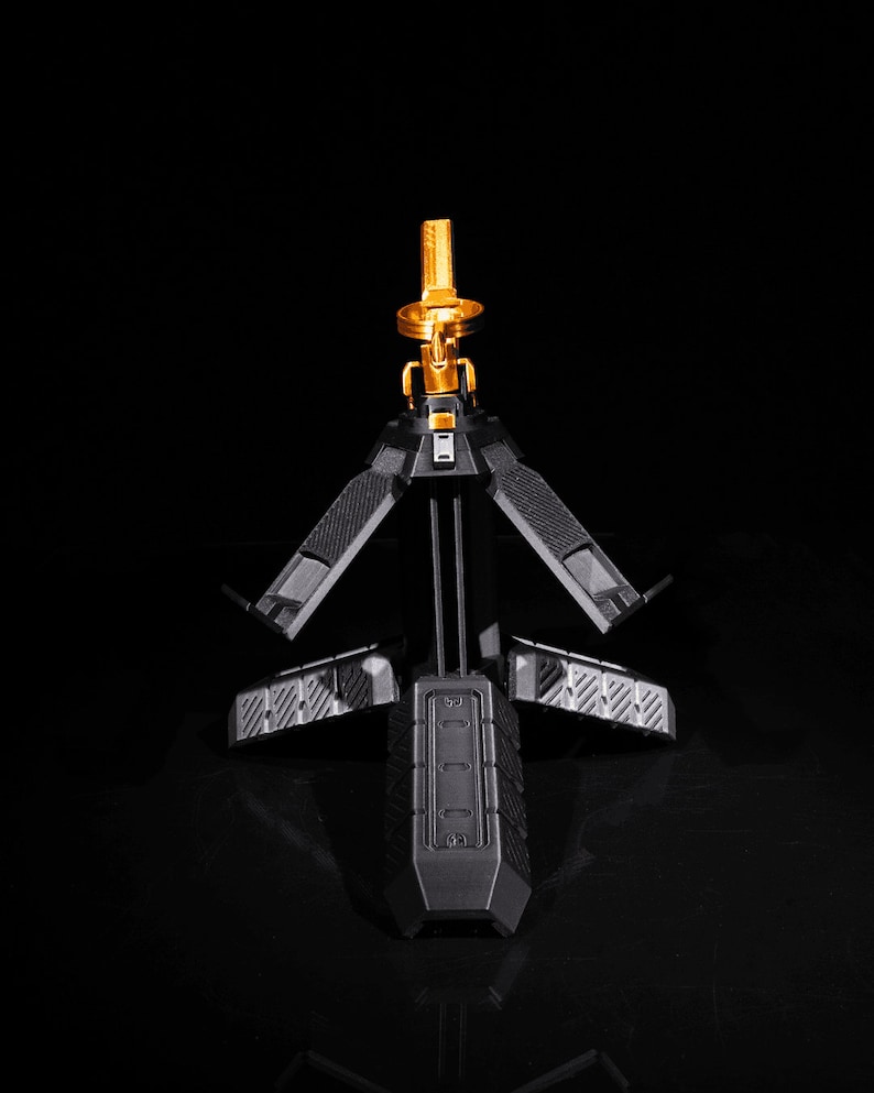 May include: A black tripod stand with a gold metal top. The tripod has three legs that fold out and a textured surface.