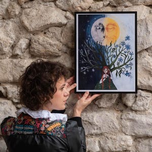 Puede incluir: Una l&aacute;mina art&iacute;stica rectangular enmarcada que muestra un rostro dividido en sol y luna sobre una figura central de pelo rojo largo. El lado izquierdo representa una noche estrellada oscura, mientras que el derecho muestra un sol con flores azules.