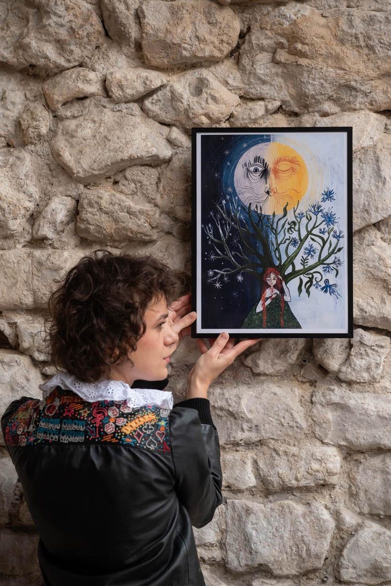 Puede incluir: Una l&aacute;mina art&iacute;stica rectangular enmarcada que muestra un rostro dividido en sol y luna sobre una figura central de pelo rojo largo. El lado izquierdo representa una noche estrellada oscura, mientras que el derecho muestra un sol con flores azules.