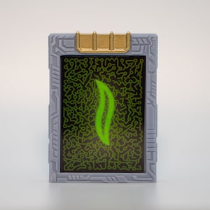 May include: A rectangular device with a gray frame and a gold accent at the top. The screen displays a green flame-like design against a black background filled with green circuit patterns. The device is set against a white backdrop.