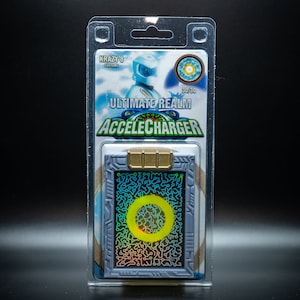May include: A packaged Accelcharger collectible card. The card is gray with a gold-colored top and a holographic design. The packaging includes the text "ULTIMATE REALM ACCELECHARGER" and "KRAZY 8 CUSTOMS".