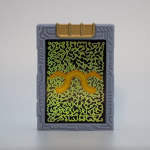 May include: A rectangular device with a gray frame and a gold accent at the top. The screen displays a neon green circuit pattern with an orange, curved design in the center. The device has a futuristic aesthetic.