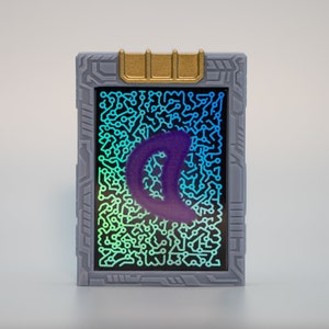 May include: A rectangular, gray device with a gold accent at the top. The screen displays a circuit board pattern with a purple, crescent-shaped design. The screen has a gradient of blue and green.
