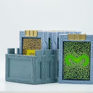 May include: A set of gray, rectangular, 3D-printed boxes with gold accents. Each box features a screen with a circuit board design in yellow or green. The boxes are arranged on a white surface.