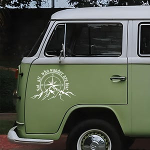 Può includere: Un furgone vintage verde chiaro e bianco con una decalcomania bianca raffigurante una rosa dei venti, montagne e la scritta "Not all who wander are lost." Il furgone ha una maniglia cromata.
