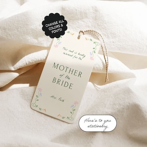 Op de afbeelding: Een wit bruiloft tafelkaartje met groene ranken en kleurrijke bloemen. De tekst luidt "Deze stoel is vriendelijk gereserveerd voor de moeder van de bruid, mevrouw Park".