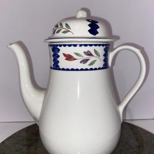 May include: White ceramic coffee pot with a blue and green floral design. The pot has a lid with a blue and green floral design.