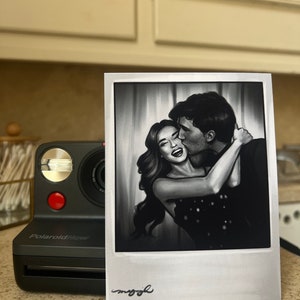 May include: A black and white Polaroid-style photo of a couple embracing. The woman is smiling and the man is kissing her cheek. The photo is framed with a white border and has the word "maggie" written in cursive at the bottom.
