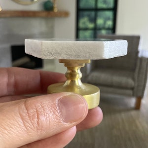 May include: A small white marble table with a gold base. The table is about 3 inches tall and 4 inches wide.