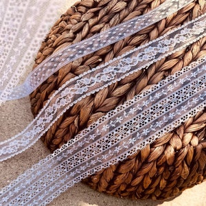 May include: Three white lace trims with different patterns, displayed on a woven basket.