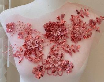 May include: A pink floral applique with sequins and beads. The applique features a cluster of pink flowers with a delicate design. The applique is perfect for adding a touch of elegance to any garment.