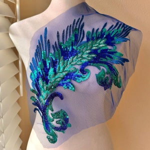 May include: A blue and green sequined applique with a feather design on a sheer blue fabric.