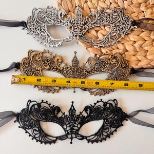 May include: Three decorative masquerade masks in silver, gold, and black. The gold mask is approximately 7 inches long. Each mask features intricate lace detailing and black ribbon ties, perfect for a costume or special event.
