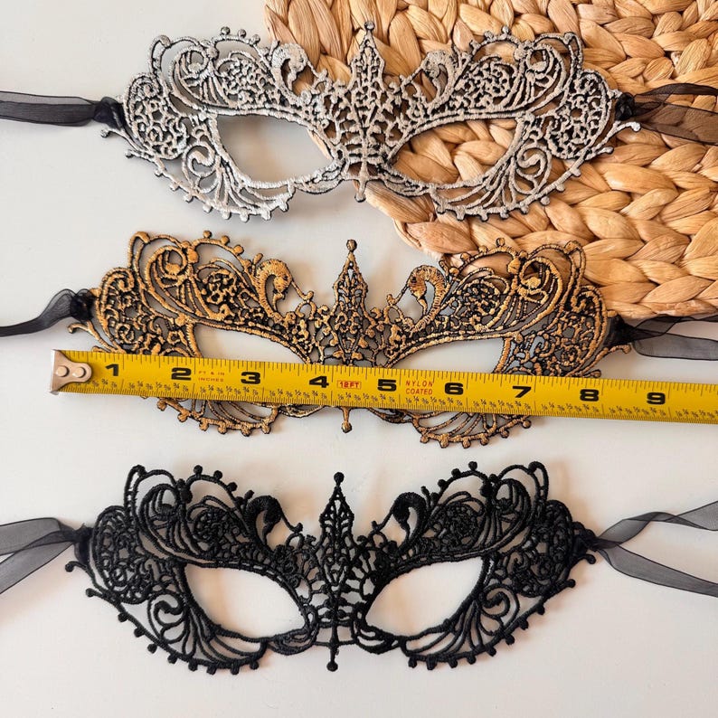 May include: Three decorative masquerade masks in silver, gold, and black. The gold mask is approximately 7 inches long. Each mask features intricate lace detailing and black ribbon ties, perfect for a costume or special event.