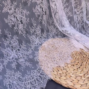 May include: White lace fabric with a delicate floral pattern. The lace is soft and sheer, and it has a slightly textured surface.