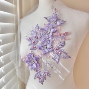 Puede incluir: Aplicación floral lavanda con detalles bordados, con flores, hojas y detalles de perlas rosas. La aplicación está adornada con brillantes pedrería y delicado encaje blanco.
