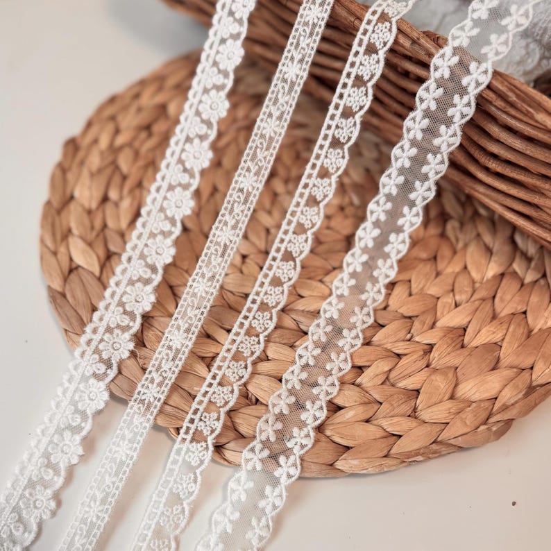May include: Four white lace ribbons with floral and geometric patterns are shown on a woven basket. The lace designs feature delicate flowers and intricate openwork, suitable for crafting and embellishments.