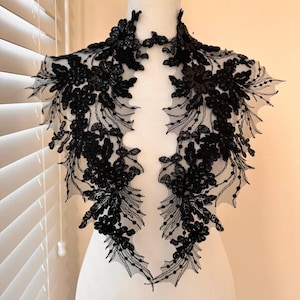 May include: Black lace trim with floral embellishments. The trim is designed to be sewn onto a garment, such as a dress or blouse.