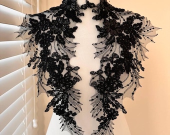 May include: Black lace trim with floral embellishments. The trim is designed to be sewn onto a garment, such as a dress or blouse.