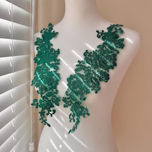 Op de afbeelding: Twee smaragdgroene bloemenkanten applicaties. De applicaties zijn ingewikkeld ontworpen met gedetailleerde bloemen- en bladerpatronen. Het kant wordt getoond op een witte mannequin, die de delicate textuur en levendige kleur van de stof benadrukt.