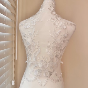 May include: White lace applique with floral and leaf patterns, displayed on a mannequin. The delicate design features detailed embroidery, creating a textured and elegant look. Ideal for bridal or formal wear.